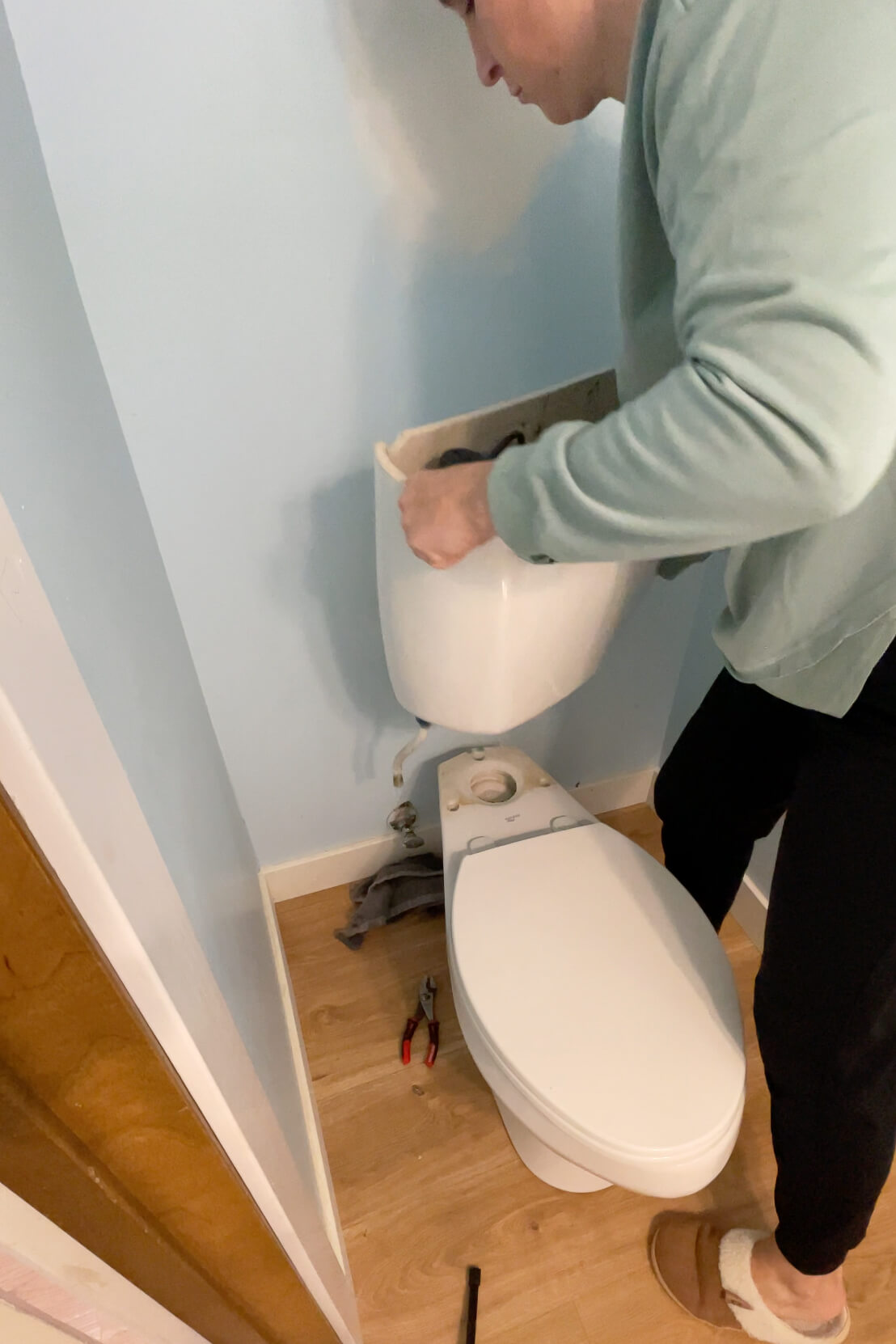 Removing the top part of the toilet in order to install beadboard on a bathroom wall.